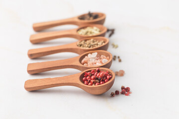 Various spices and green herbs in wooden spoons on white table