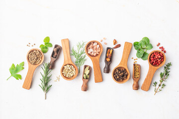 Various spices and green herbs in wooden spoons on white table