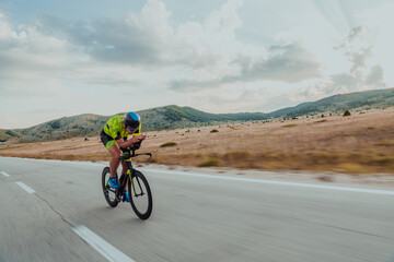 Fototapeta premium Full length portrait of an active triathlete in sportswear and with a protective helmet riding a bicycle. Selective focus 