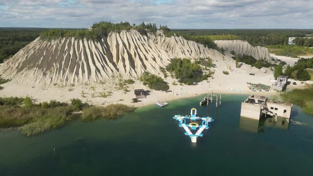 Crystal clear light blue lagoon of Rummu quarry and the adjacent ash hill. Drone shot of white sand mountain by the construction site. Beautiful white sand beach bathed by a turquoise water. 