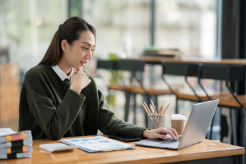 Young Asian businesswoman holding a pen sitting and analyzing the details of management information Finance is happy at the desk in the office. © crizzystudio