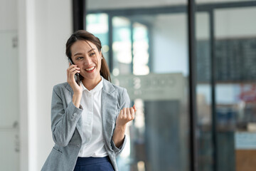 Attractive Asian businesswoman standing on the phone talking about real estate projects and chatting with happy smiles at the office.