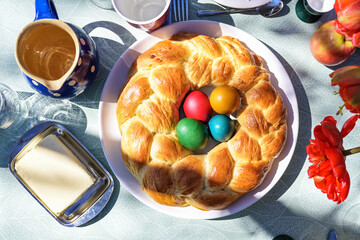 Traditional Easter plait in wreath shape baked from a slightly sweet yeast dough with colorful eggs in the center on a set table outside in the sun, high angle view from above