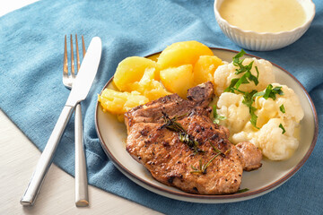 Dish with pork chop, cauliflower, potatoes and hollandaise sauce served with herb garnish on a plate and a blue napkin, selected focus