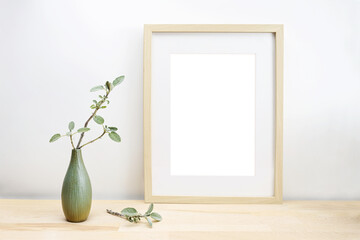 Empty wooden picture frame with passe-partout as mock-up and a vase with sage twig on a light table...