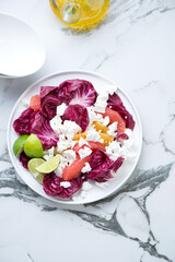 Plate with radicchio, goat cheese and citrus salad on a white marble background, vertical shot with space, top view