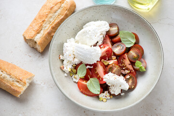 Salad with red tomatoes, ricotta, chopped pistachios and fresh green basil, horizontal shot on a light-beige stone background