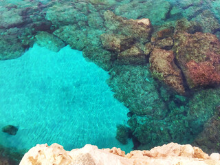 Lagre stones in the blue water. Rocky bottom of the sea with white sand. Top view from the cliff.