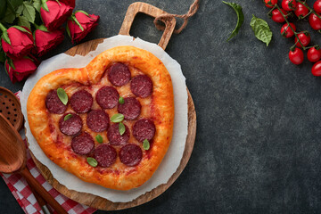 Valentines day heart shaped pizza with mozzarella, pepperoni and basil, wine bottle, two wineglass, gift box on black background. Idea for romantic dinner Valentines day. Top view. Mock up.
