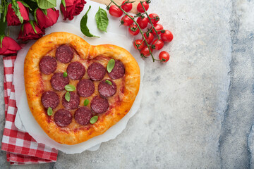 Valentines day heart shaped pizza with mozzarella, pepperoni and basil, wine bottle, two wineglass, gift box on light grey background. Idea for romantic dinner Valentines day. Top view. Mock up.
