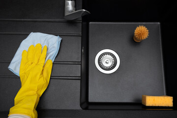 New granite kitchen sink black. Cleaning female hand washes the sink with a rag without traces