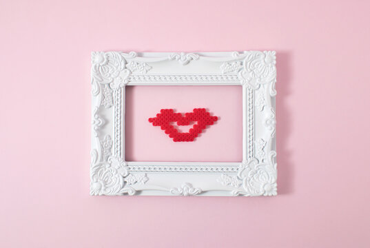 White vintage frame with kiss on pastel pink background. Minimal love composition.