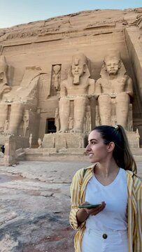Vertical view of young smiling tourist woman taking a selfie in the facade entrance of the Abu simbel temple in Egypt