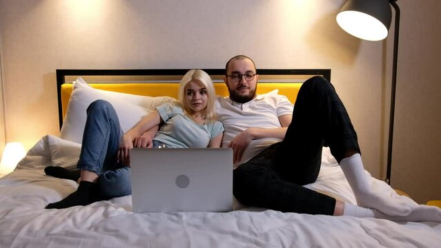 Happy relaxed young couple lying on sofa and watching film, photos or TV series on laptop