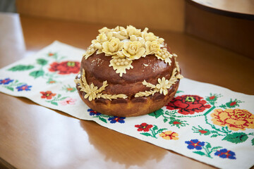 Ukrainian traditional holiday bread - loaf. Ukrainian decorated fresh loaf with salt lies on the table, next to the embroidered towel. Ukrainian wedding traditions.