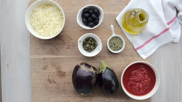 Mano de mujer coge un rulo de jam&oacute;n serrano de una tabla de madera con ingredientes de una receta de pizzas de berenjena.
