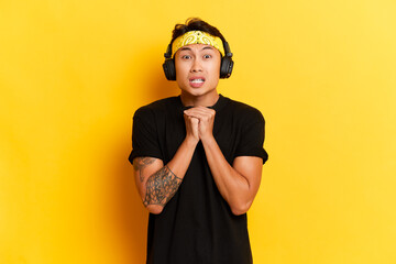 Scared asian man listens music via black wireless headphones finds out something horrible listening...