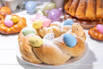 Easter wreath bread, traditional Easter holiday baking, sweet bun cakes with colorful Easter eggs, on brunch holiday decorated table copy space
