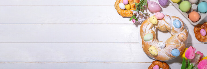 Easter wreath bread, traditional Easter holiday baking, sweet bun cakes with colorful Easter eggs, on brunch holiday decorated table copy space