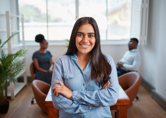 Fototapeta premium Young Indian business woman stands arms folded in boardroom, diverse colleagues
