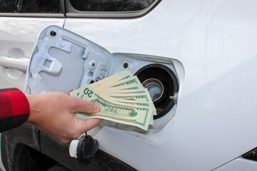 Mans hand placing US dollars into a gas tank. Rise of fuel costs concept shot.