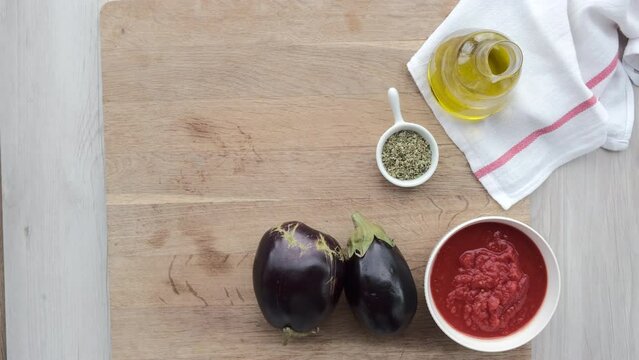 Mano de mujer coge un bol de or&eacute;gano de una tabla de madera con ingredientes de una receta de pizzas de berenjena.
