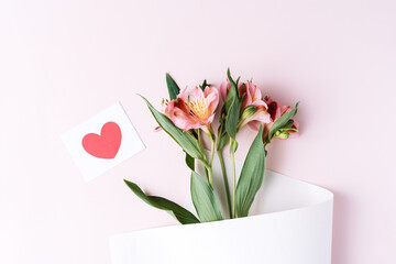 Alstroemeria in paper packaging with a postcard on a pink background.