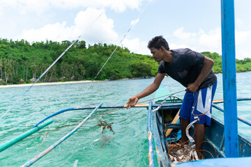 Asian fisherman picking up his fishing net on a small boat at sea, Philippines islands , lifestyle