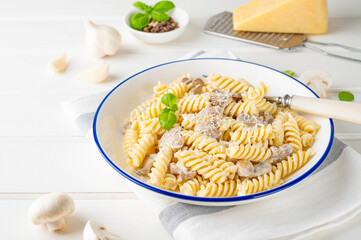 Fusilli pasta with mushrooms, cheese and fresh basil in a plate on a white wooden background.