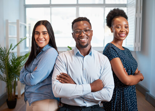 Group of smiling business people pose arms folded in office, diverse trio