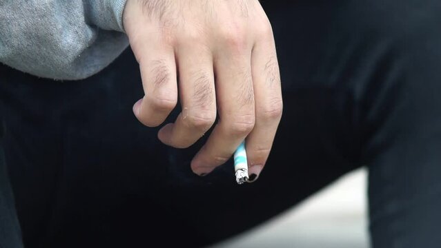 Mano de joven sosteniendo un cigarro en un plano detalle. Hombre fumando un cigarrillo en detalle