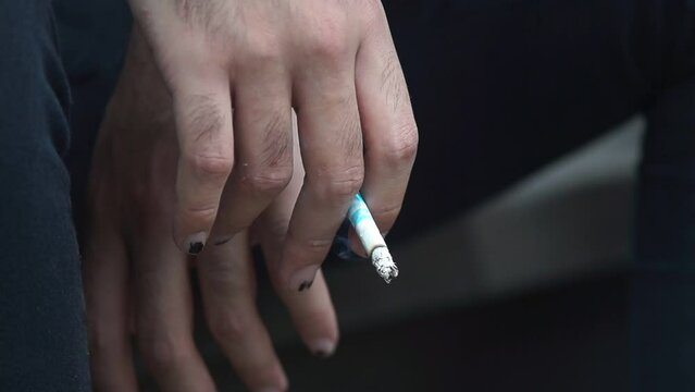 Mano de joven adulto con las u&ntilde;as pintadas de negro, sosteniendo un cigarro en un plano detalle. Hombre fumando un cigarro detalle de la mano.