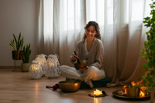 Happy young woman playing singing bowl during meditation