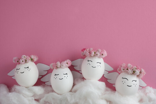 Angels made of eggs in wreath of flowers on clouds. Easter egg. Pink background. Space for text.