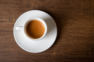 White cup of espresso on wooden table, top view

