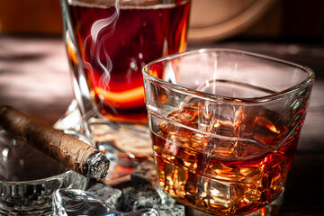A glass of scotch whiskey with ice and a cigar on a wooden table close-up.