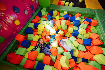 Brother with sister playing at indoor play center playground in color cubes pool.