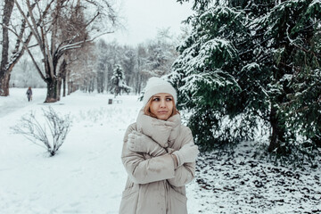Obraz premium A girl in a beige coat is freezing against the backdrop of a winter forest