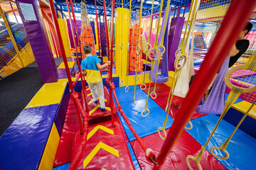 Happy kids playing at indoor play center playground,  boy climbs the ropes.
