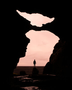 Girl stands on a rock in a famous Yoda cave (G&iacute;gjagj&aacute;) with beautiful pink sky with clouds. Iceland hidden gems - Hj&ouml;rleifsh&ouml;f&eth;i mountains