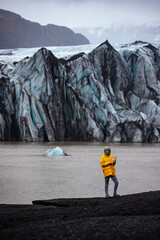 Happy girl in yellow raincoat holding ice chunk from the  outer glacier Mýrdalsjökull on...