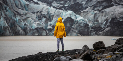 Beautiful girl in a yellow raincoat admires the powerful big Katla glacier during rainy weather in southern Iceland