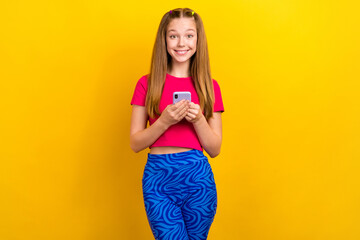 Photo of satisfied schoolgirl blond hair pink t-shirt hold phone facebook instagram twitter whatsapp isolated on yellow color background