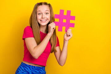 Photo of young teen age girl smiling hold paper hashtag pin social media popular enjoy blogging instagram symbol isolated on yellow color background