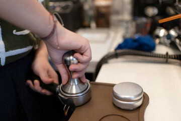 Hands using metal tamper tamping ground coffee to make coffee. Barista tamping by tamper with manual presses on coffee bar at coffeeshop or cafe. Coffee maker concept.