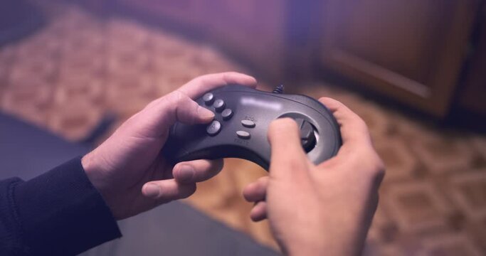 Retro video game joysticks in male hands, close up. Man playing in old controller, mashing buttons. Magenta light from tv screen. Nostalgic console fun gaming in room. Vintage digital entertainment