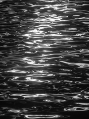 Momentary reflections of morning sunlight on rippled water in a calm harbor, in black and white,...