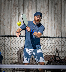 Young pickleball man about to slice a whiffle ball over the net.