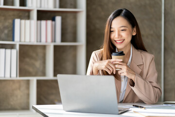 Beautiful Asian businesswoman smiling confident and bright ready to work on a new day with a cup of coffee. Please be ready to work with laptops and financial graphs in front of you.