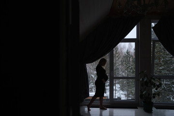Fototapeta premium The Silhouette of Pregnant woman standing against the window